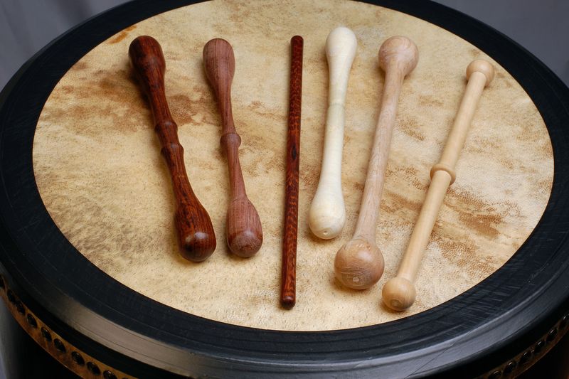Six bodhrán tippers of different woods, lengths and shapes lying on a drum head